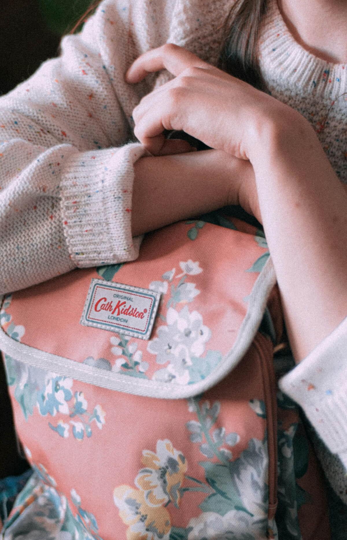 Young person hugging a small floral patterned book bag between their arms